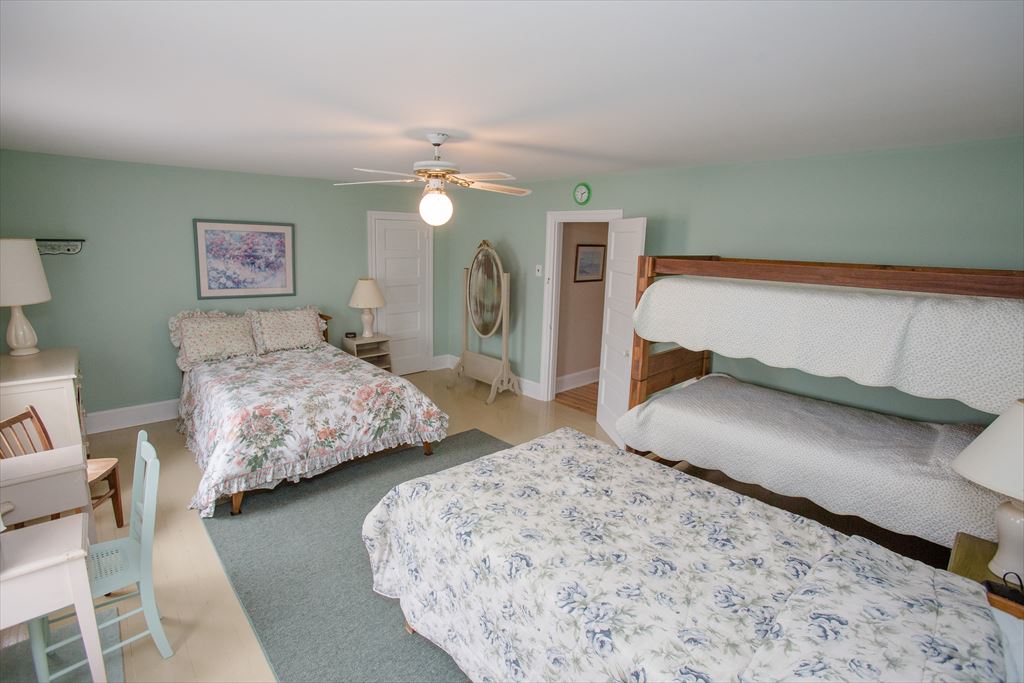 Green-walled bedroom with a full bed in floral bedding, a wood bunk bed, a white desk and a ceiling fan
