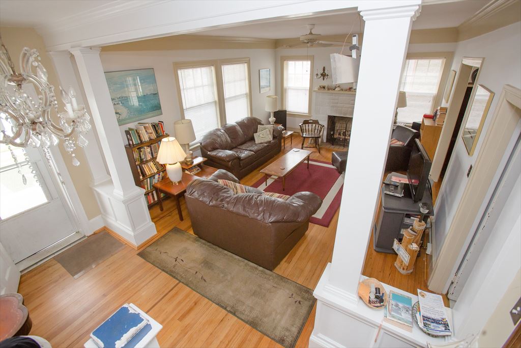 Elevated view of the living room with brown leather sofas, bookshelves, a crystal chandelier near the glass entry door and hardwood floors