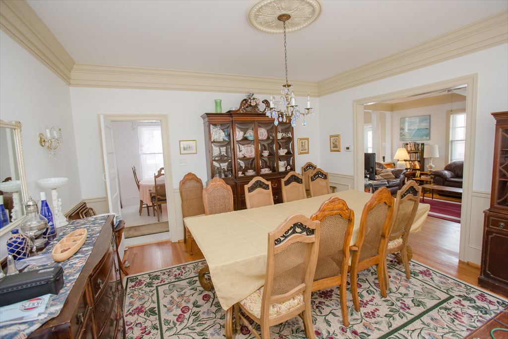 Formal dining room with a long wood table and caned chairs, an antique china cabinet, a ceiling medallion and chandelier, open to the living room