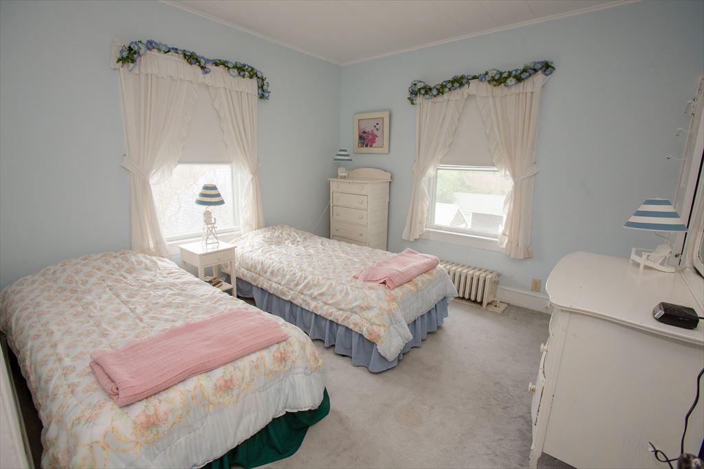 Pale blue bedroom with two twin beds in floral spreads, white dressers and ruffled sheer curtains