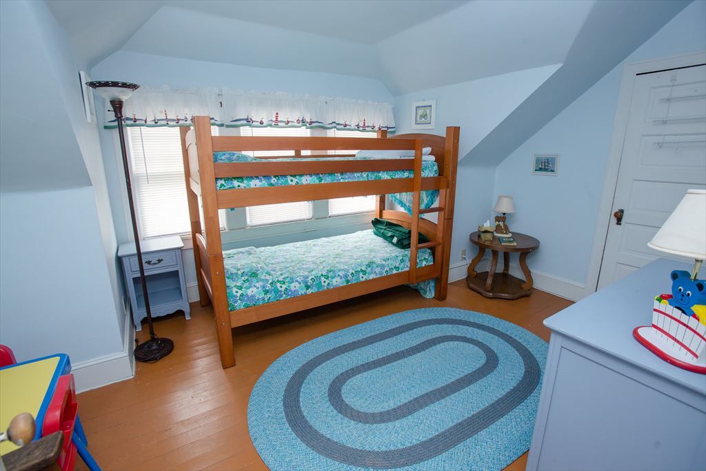 Light blue children's bedroom with a wooden bunk bed in floral bedding, a lighthouse-print valance and toy bins