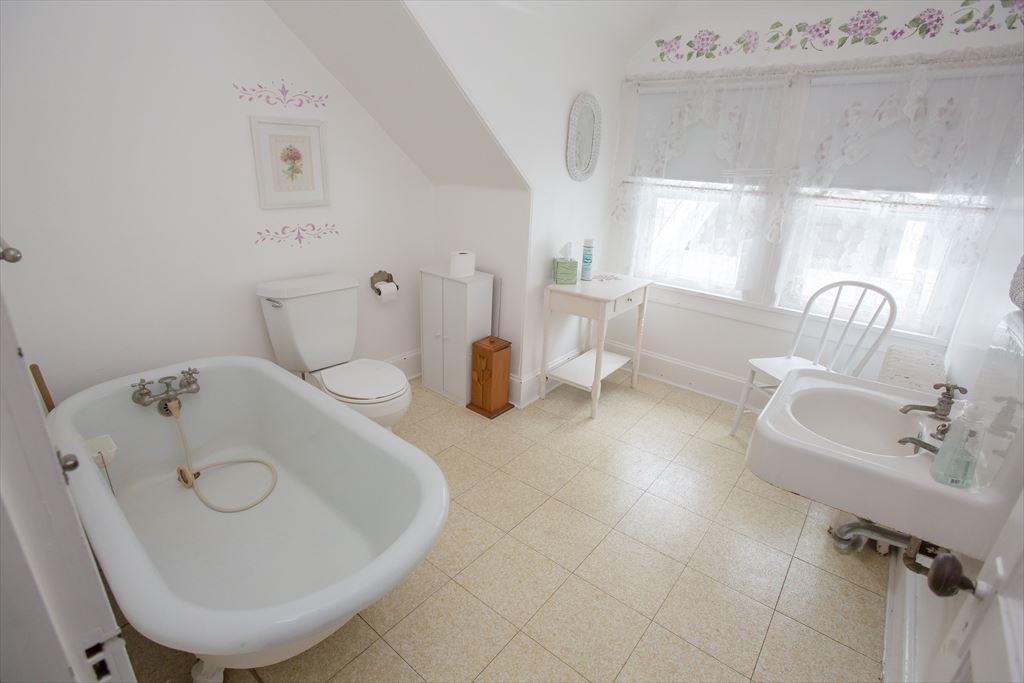 Spacious upstairs bathroom with a sloped ceiling, an antique claw-foot tub, a pedestal sink and lace curtains