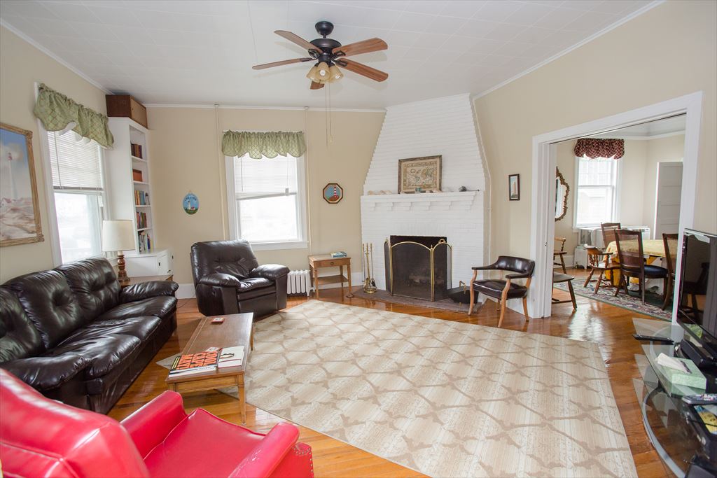 Living room with a dark leather sofa and recliner, a red accent chair, a white painted brick fireplace and hardwood floors